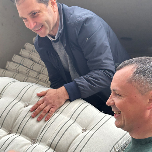 2 smiling men unload mattresses from a truck